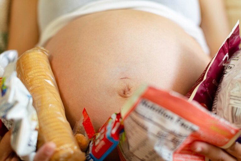A pregnant woman holding many snacks and food cravings around her baby belly.