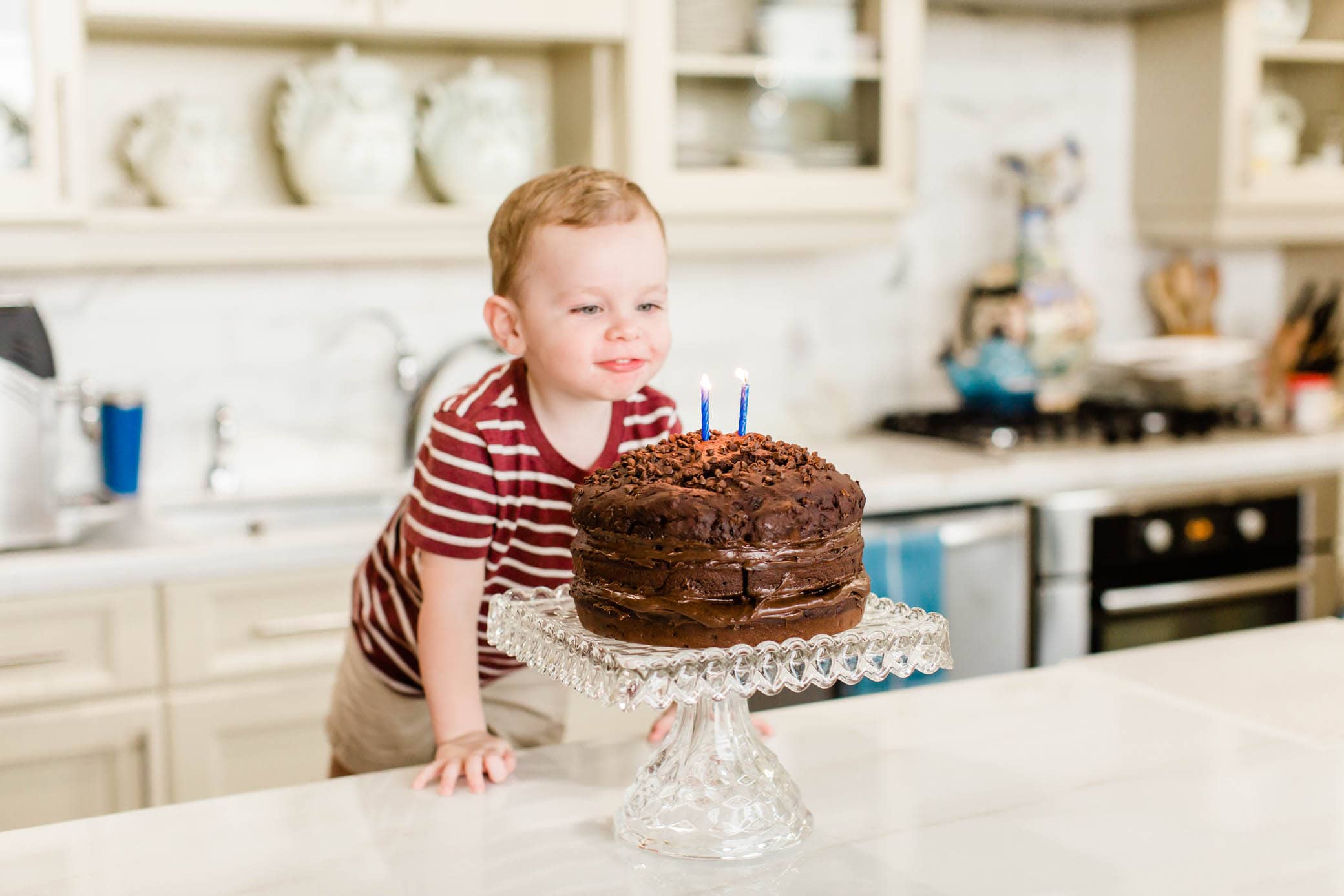 Toddler boy blowing out his candles on his chocolate birthday cake