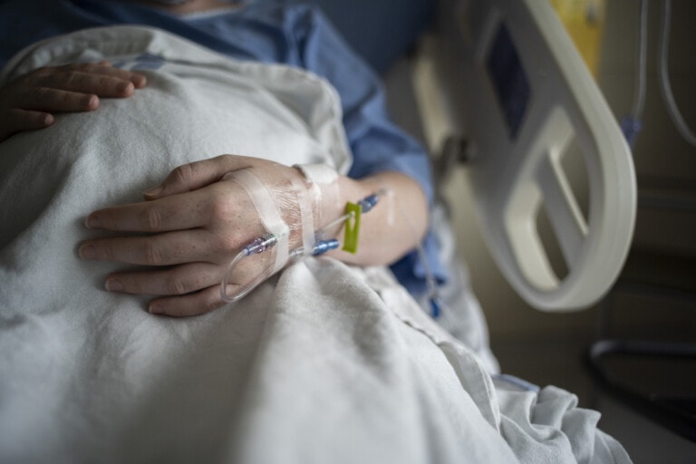 A pregnant hospital patient is receiving intravenous therapy in their hand.