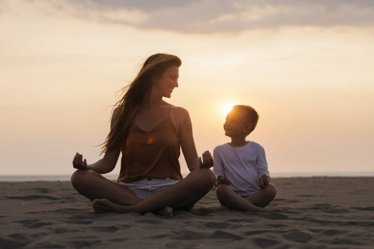 Mom and her young son happy to do to yoga together at sunset by the sea.