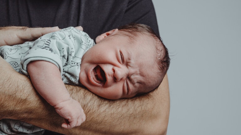 newborn on his father's arm screams crying with expression of suffering